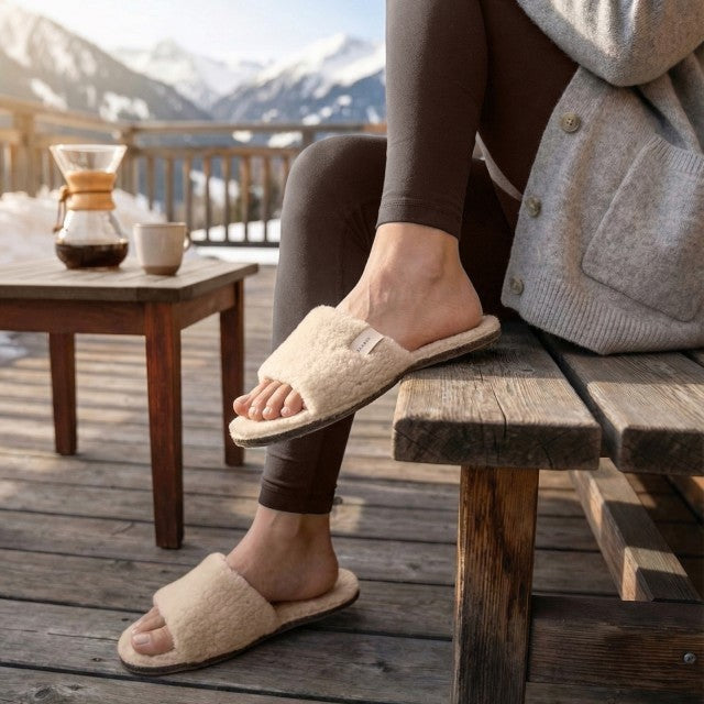 Baabuk Baabulette Fluffy wool slide sandals in cream, worn on a wooden deck with a mountain view.