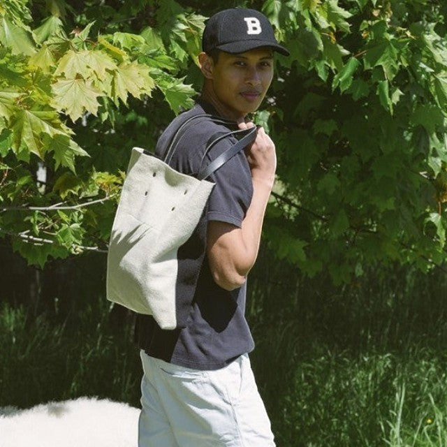 Baabuk Blacknose tote bag in cream wool and leather worn over the shoulder by a man in a park setting.