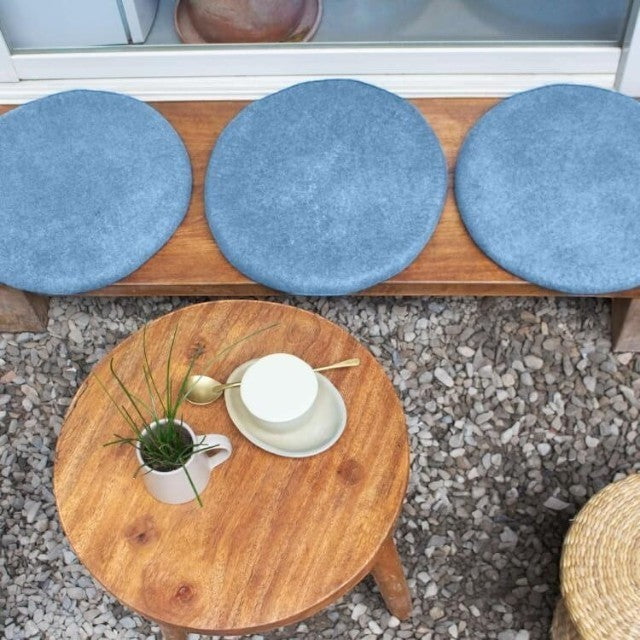Baabuk handmade blue wool felt sitting mats arranged on a wooden bench next to a small round table.