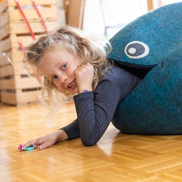 A young girl playing with a blue Baabuk wool whale storage basket in a bright room.