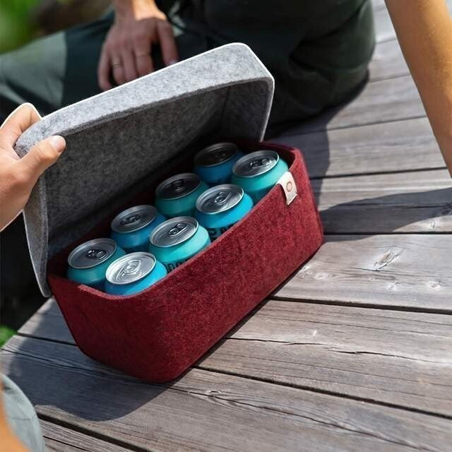 Baabuk bordeaux wool beer cooler holding six cans on a wooden deck with a grey lid being opened