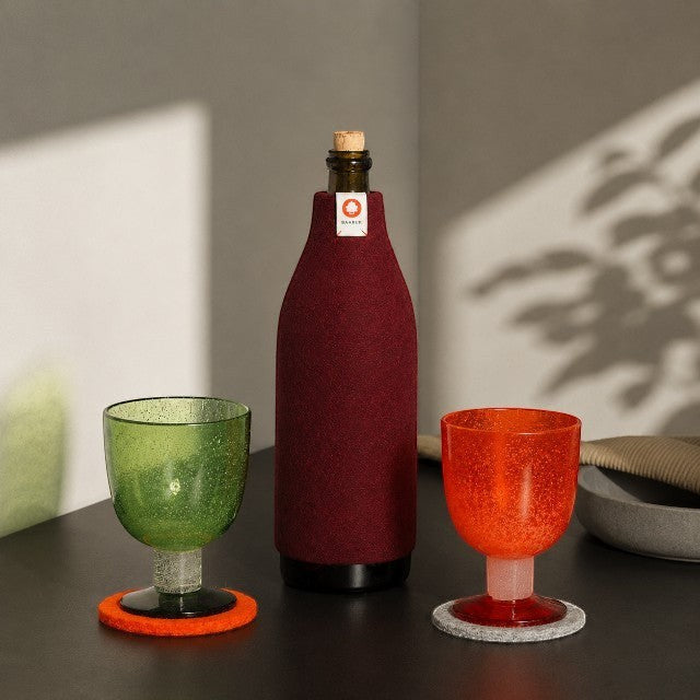 Baabuk bordeaux wool bottle cover insulating a glass bottle next to colorful glasses on a table