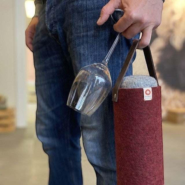 Baabuk Bordeaux wool wine cooler with a leather strap, held by a person carrying a wine glass.
