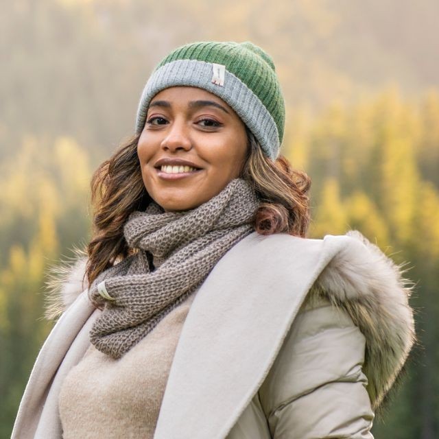 Baabuk model wearing a brown baby alpaca infinity scarf and a green and grey ribbed beanie in a forest setting