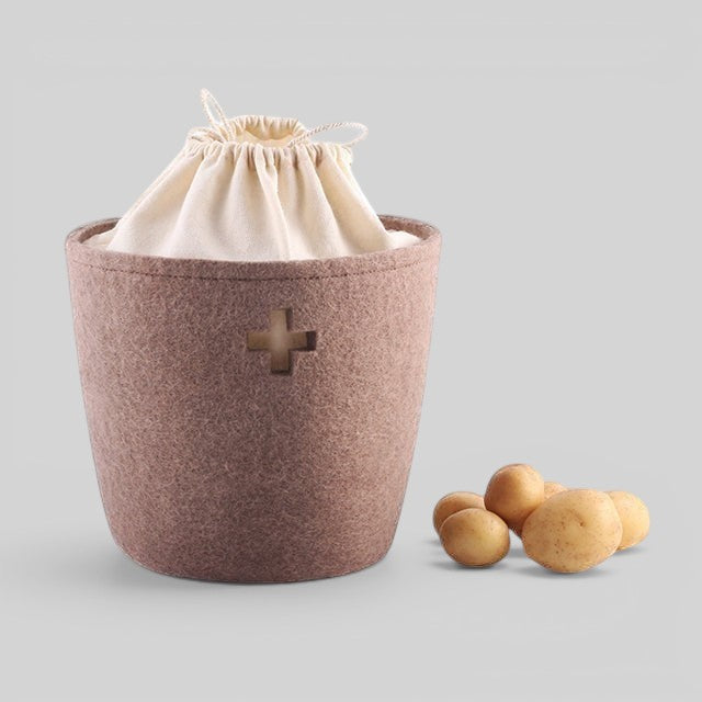 Baabuk small brown felted wool basket with a cream drawstring liner and Swiss cross cutout, holding potatoes.