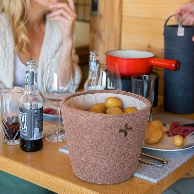 Baabuk large brown felted wool basket with Swiss cross cutout, holding potatoes on a dining table.