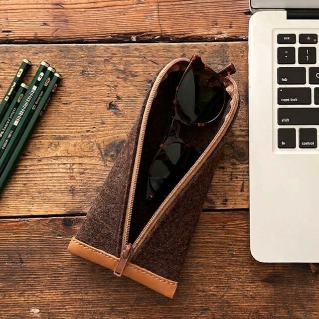 Baabuk brown wool pencil case with leather accents containing sunglasses on a wooden desk next to a laptop.