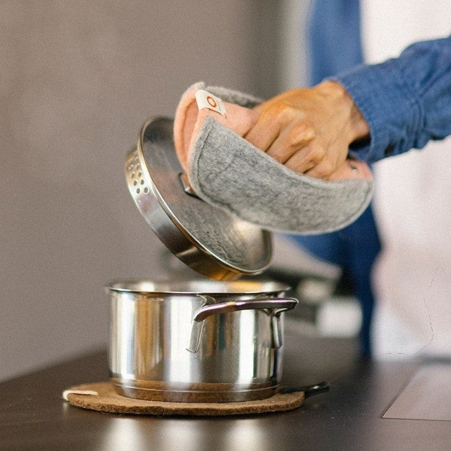 Baabuk brown felted wool trivet under a stainless steel pot with a person using a grey wool pot holder