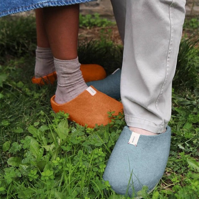 Baabuk Corkybuk wool slippers in terracotta and blue worn by two people standing on green grass