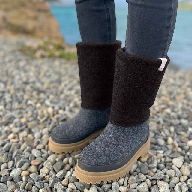 Baabuk Dani boots in dark grey felted wool with a thick tan rubber sole, worn outdoors on a rocky beach.