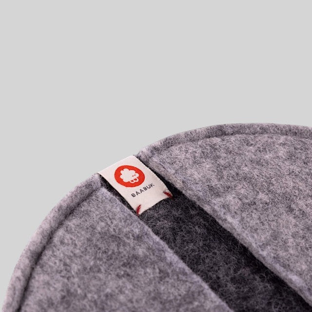 Baabuk dark grey felted wool potholder with a small branded fabric tag featuring a red logo
