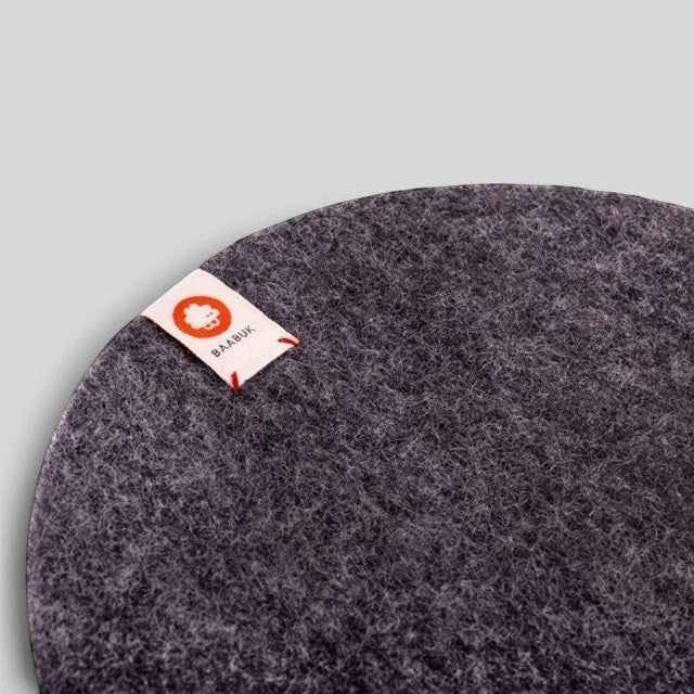 Baabuk dark grey felted wool trivet hot plate with a small branded leather strap detail for kitchen surface protection.