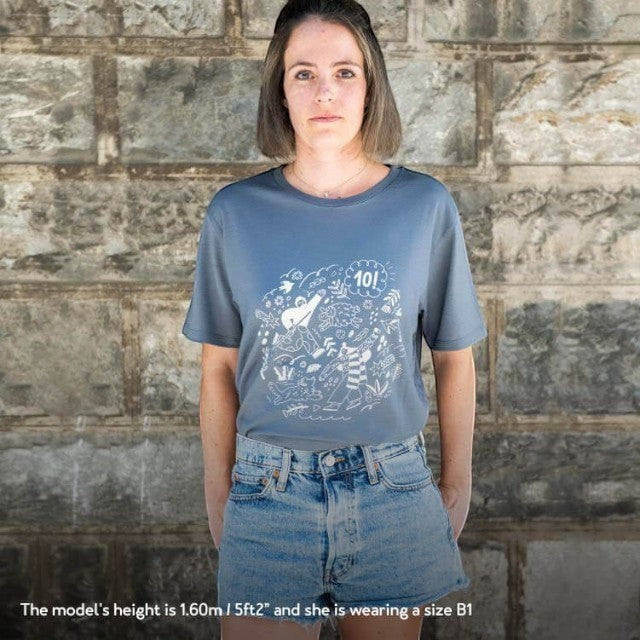 A woman wearing a dark grey Baabuk 10-year anniversary merino wool T-shirt with a white Portuguese-themed illustration.