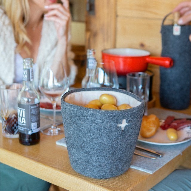 Baabuk small dark grey felted wool basket with a Swiss cross cutout, sitting on a wooden dining table.