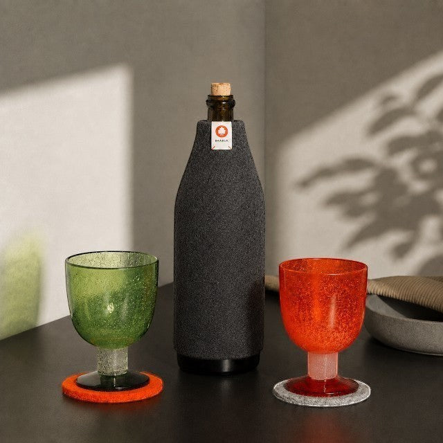Baabuk dark grey wool bottle cover insulating a bottle next to green and orange glasses on a table