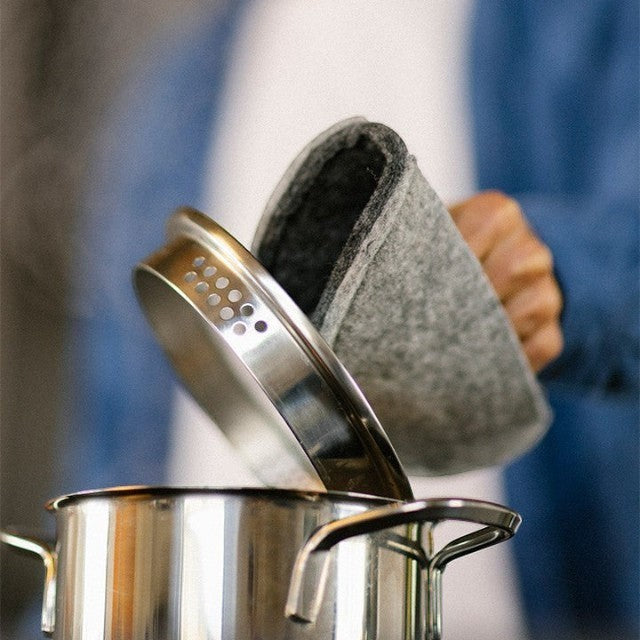 Baabuk dark grey felted wool potholder being used to lift a hot stainless steel pot lid in a kitchen setting