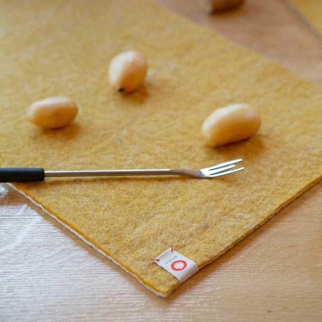 Baabuk honey yellow felted wool table mat with a fork and potatoes on a wooden dining table