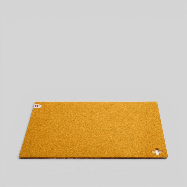 Baabuk honey yellow felted wool table mat with a small Swiss cross cutout detail on a neutral background.