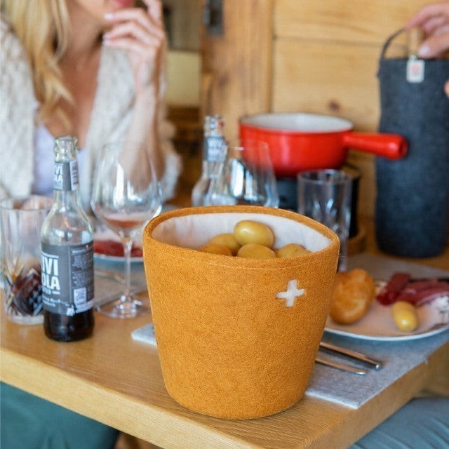 Baabuk honey felted wool basket with a Swiss cross cutout, holding potatoes on a dining table.