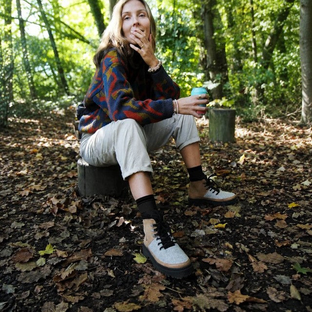 Baabuk Ice Wooler pepper brown wool boots worn by a woman sitting on a tree stump in a forest setting