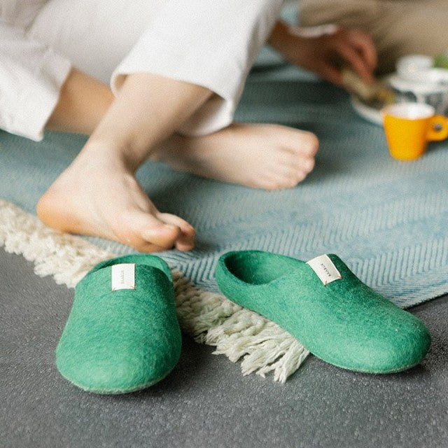 Baabuk Kanga slippers in lush green felted wool, handmade in Nepal, resting on a textured rug.