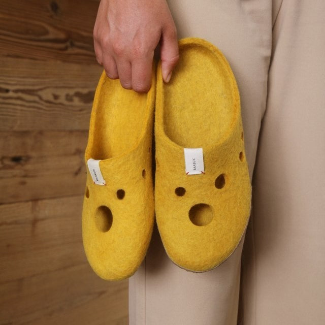 Baabuk Kanga Swiss Cheese yellow wool slippers with playful hole cutouts held by hand