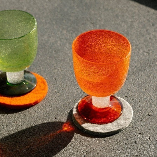 Baabuk khaki felted wool coaster under an orange textured glass on a grey surface