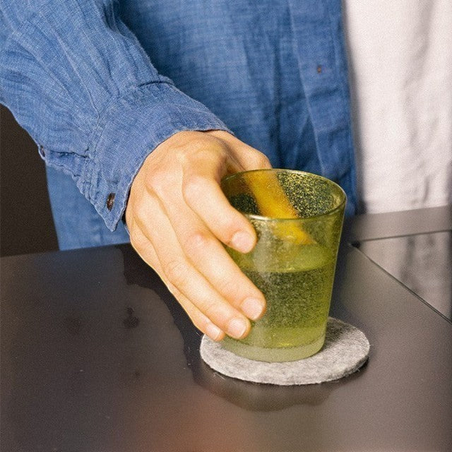 Baabuk khaki felted wool coaster under a glass on a dark table, showcasing sustainable New Zealand wool design.