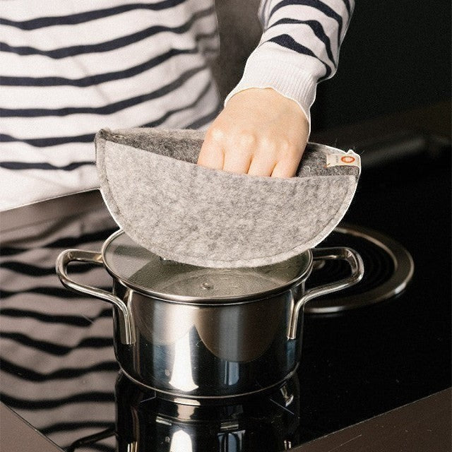 Baabuk khaki felted wool potholder with a leather strap being used to lift a hot pot lid on a stovetop
