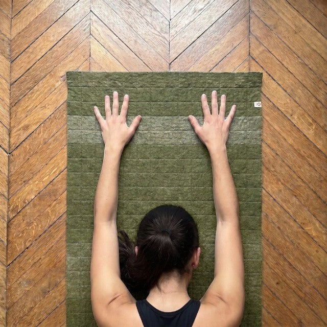 Baabuk khaki felted wool yoga mat with cotton stitching and anti-slip underside, viewed from above during practice.