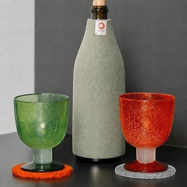 Baabuk khaki wool bottle cover insulating a glass bottle next to green and orange textured glasses on felt coasters