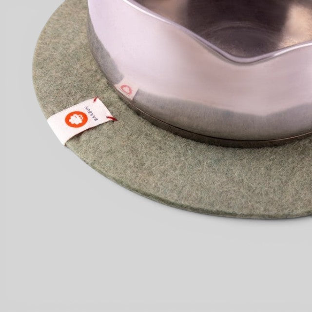Baabuk khaki felted wool trivet hot plate with a small leather strap detail under a stainless steel pot.