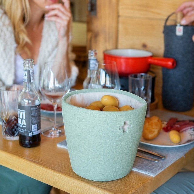 Baabuk small light blue felted wool basket with Swiss cross cutout on a dining table with food and drinks