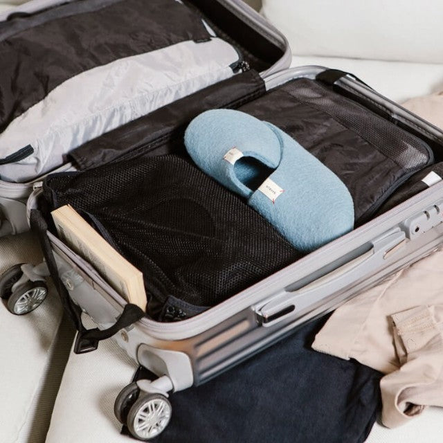 Baabuk light blue wool Kanga slippers packed inside a travel suitcase with clothing and a book.