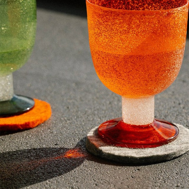 Baabuk light grey felted wool coaster under an orange glass on a dark textured surface