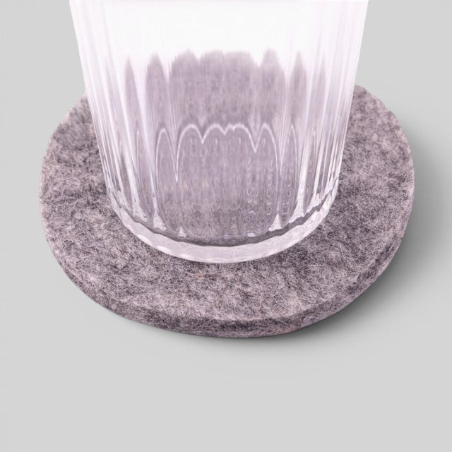 Baabuk round light grey felted wool coaster under a clear glass on a neutral background