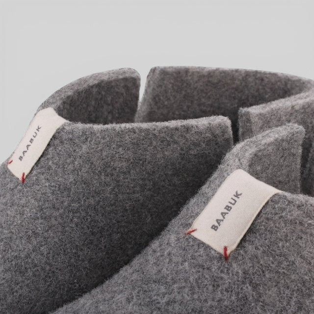 Close-up of Baabuk Lisa light grey wool slippers showing the felt texture and branded fabric pull tabs.