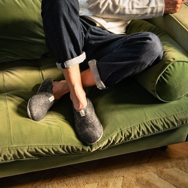 Baabuk Mel dark grey wool slippers with natural crepe rubber soles worn by a person sitting on a green velvet sofa