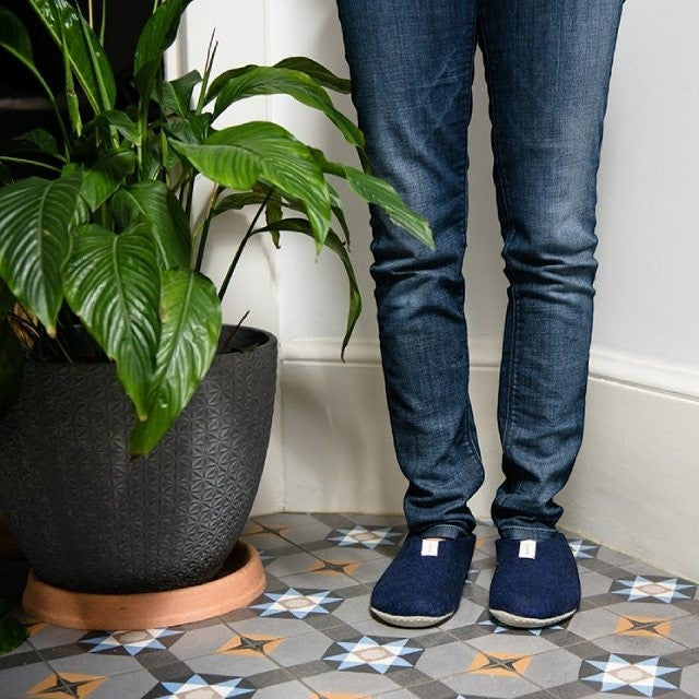 Baabuk Mel navy blue wool slippers worn with jeans on a patterned tile floor next to a potted plant.