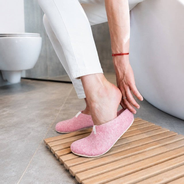 Baabuk Mel pink wool slippers with natural crepe rubber soles being put on by a person in a bathroom setting.