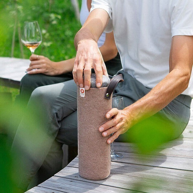 Baabuk moka wool wine cooler with leather strap being used by a person on a wooden bench during an outdoor picnic.