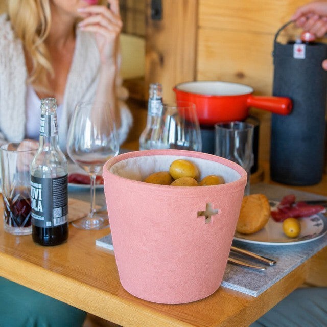Baabuk small pink felted wool basket with Swiss cross cutout on a dining table with food and drinks.