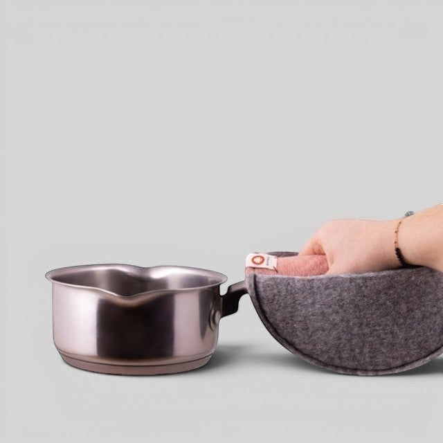 Baabuk pink felted wool potholder with a leather strap, shown in use gripping a stainless steel saucepan.