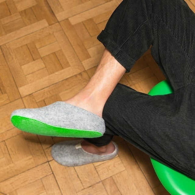Baabuk Pomobuk slippers in grey wool with a bright green upcycled ski-skin sole worn by a person on a wooden floor.