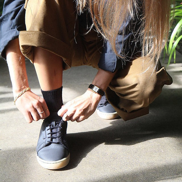 Person crouching to tie black Baabuk Shunya Wooler sneakers made from sustainable wool and plant-based materials.