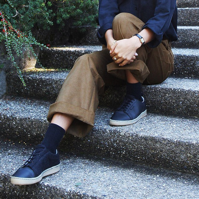 Baabuk Shunya Wooler black wool sneakers worn by a person sitting on stone steps with brown trousers.