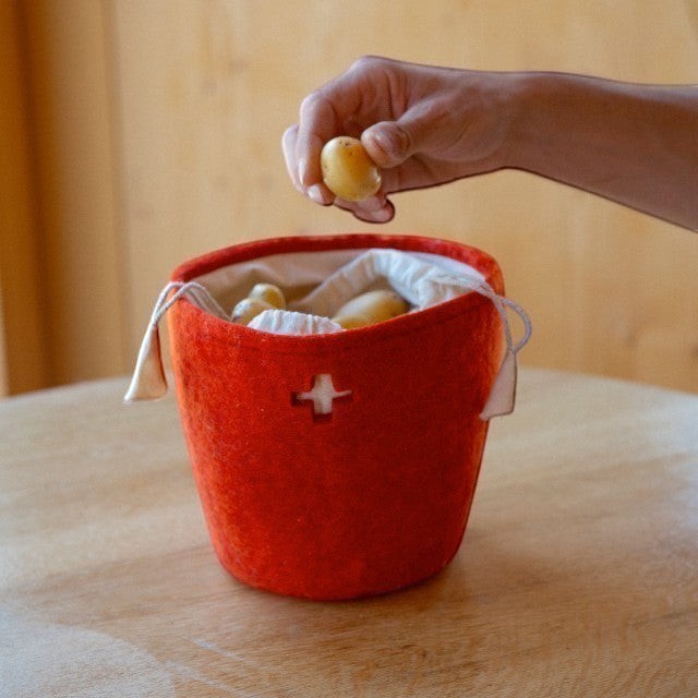 Baabuk small Swiss red felted wool basket with leather strap holding potatoes on a wooden table