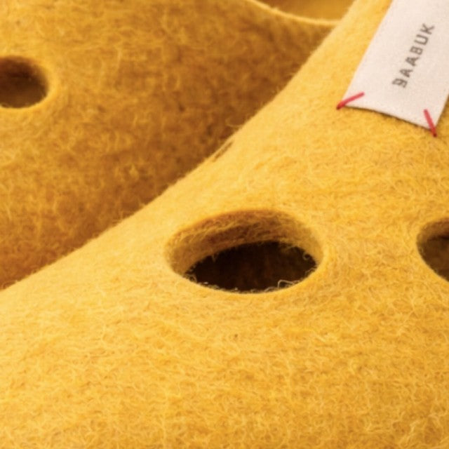 Baabuk Swiss Cheese wool slippers in vibrant yellow with playful hole details and branded fabric tag