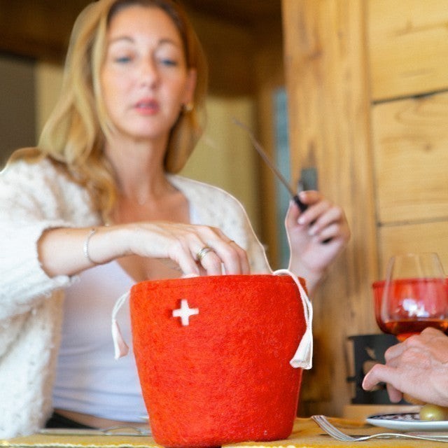 Baabuk Swiss Red felted wool basket with white cross detail on a dining table with a woman in the background.