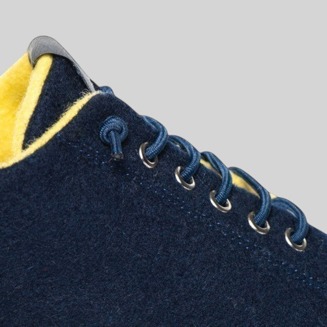 Baabuk Urban Wooler sneaker in navy blue wool with bright yellow lining and elastic laces, close-up view.
